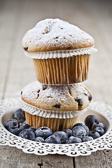 Image showing Two homemade fresh muffins with sugar powder and blueberries on 