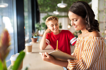 Image showing woman with friend at cafe writing to notebook