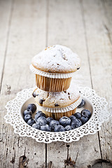 Image showing Two homemade fresh muffins with sugar powder and blueberries on 