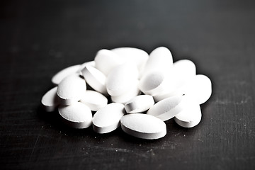 Image showing Pile of white drug pills laying on black board background.