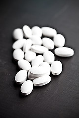 Image showing Pile of white drug pills laying on black board background.