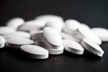 Image showing Pile of white drug pills laying on black board background.