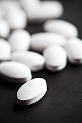 Image showing Pile of white drug pills laying on black board background.