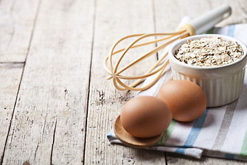 Image showing Fresh chicken eggs, oat flakes in ceramic bowl and kitchen utens