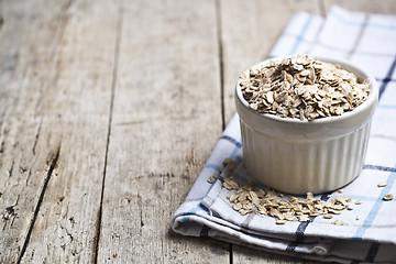 Image showing Oat flakes in ceramic bowl on linen napkin, golden wheat ears on