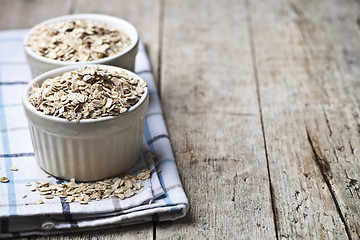 Image showing Oat flakes in ceramic bowls on linen napkin, golden wheat ears o