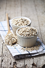 Image showing Oat flakes in ceramic bowls and wooden spoon, golden wheat ears 