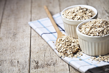 Image showing Oat flakes in ceramic bowls and wooden spoon on linen napkin, go