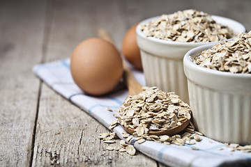 Image showing Fresh chicken eggs, oat flakes in ceramic bowl and wooden spoon 