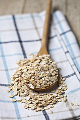 Image showing Oat flakes in wooden spoon on linen napkin, golden wheat ears on