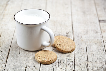 Image showing Cup of milk and some fresh baked oat cookies on rustic wooden ta