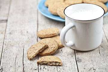 Image showing Cup of milk and fresh baked oat cookies on blue ceramic plate on