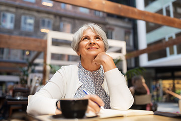 Image showing senior woman with notebook dreaming at street cafe