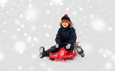 Image showing happy boy sliding on sled down snow hill in winter