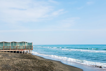 Image showing Beautiful sea, the black sandy beach and white and blue striped beach houses