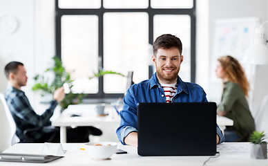 Image showing smiling creative man with laptop working at office