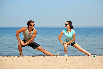 Image showing smiling couple stretching legs on beach