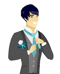 Image showing Young asian cheerful groom adjusting tie.