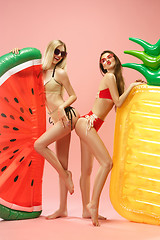 Image showing Cute girls in swimsuits posing at studio. Summer portrait caucasian teenagers on pink background.