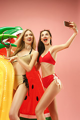 Image showing Cute girls in swimsuits posing at studio. Summer portrait caucasian teenagers on pink background.