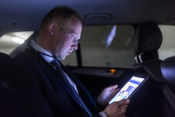 Image showing Businessman with a digital tablet sitting in the back seat of a car