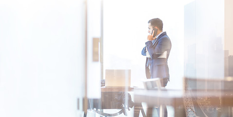 Image showing Businessman talking on a mobile phone in corporate office while looking through window.