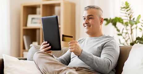 Image showing man with tablet pc and credit card on sofa at home