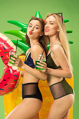 Image showing Cute girls in swimsuits posing at studio. Summer portrait caucasian teenagers on green background.