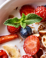 Image showing Fresh milk with homemade honey granola and natural organic ingredients - berries, nuts and mint in the white ceramic bowl. Close-up.