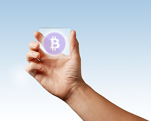 Image showing A man\'s hand holds a transparent digital screen with a bitcoin icon ns blue background