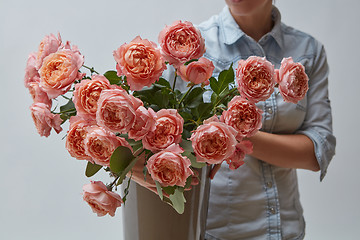 Image showing A bouquet of fresh pink roses in a brown vase holds a girl in her hands