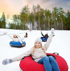 Image showing happy friends sliding down hill on snow tubes