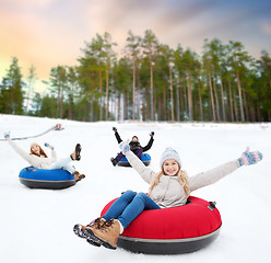 Image showing happy friends sliding down hill on snow tubes