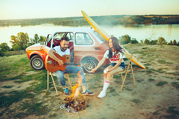 Image showing Couple sitting and resting on the beach playing guitar on a summer day near river