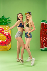 Image showing Cute girls in swimsuits posing at studio. Summer portrait caucasian teenagers on green background.