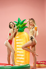 Image showing Cute girls in swimsuits posing at studio. Summer portrait caucasian teenagers on pink background.