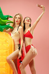 Image showing Cute girls in swimsuits posing at studio. Summer portrait caucasian teenagers on pink background.