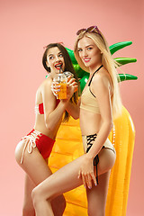 Image showing Cute girls in swimsuits posing at studio. Summer portrait caucasian teenagers on pink background.