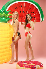 Image showing Cute girls in swimsuits posing at studio. Summer portrait caucasian teenagers on pink background.