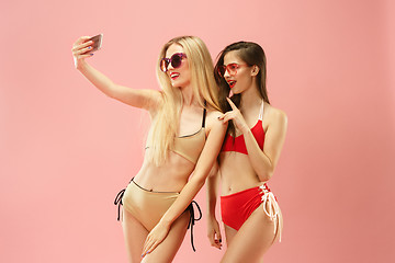 Image showing Cute girls in swimsuits posing at studio. Summer portrait caucasian teenagers on pink background.