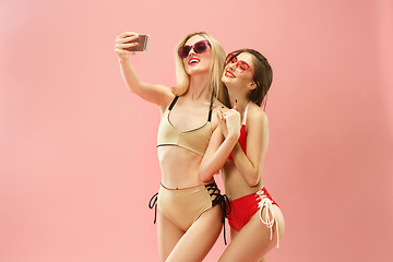 Image showing Cute girls in swimsuits posing at studio. Summer portrait caucasian teenagers on pink background.