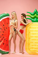 Image showing Cute girls in swimsuits posing at studio. Summer portrait caucasian teenagers on pink background.