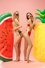 Image showing Cute girls in swimsuits posing at studio. Summer portrait caucasian teenagers on pink background.