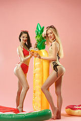 Image showing Cute girls in swimsuits posing at studio. Summer portrait caucasian teenagers on pink background.