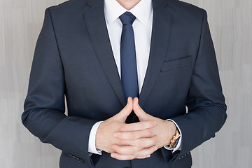 Image showing Torso of anonymous businessman standing with hands in lowered steeple, wearing beautiful fashionable classic navy blue suit.