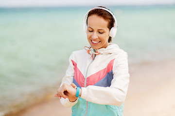 Image showing woman with fitness tracker and headphones on beach