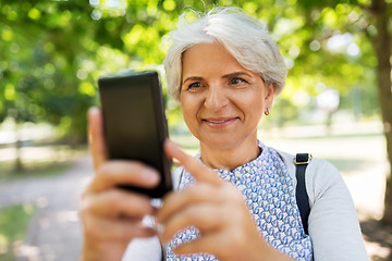 Image showing senior woman photographing by cell at summer park