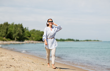 Image showing woman with headphones walking along summer beach