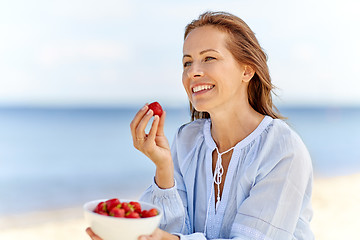 Image showing happy woman eating strawberries on summer beach