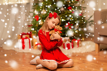 Image showing girl in red dress hugging teddy bear at home